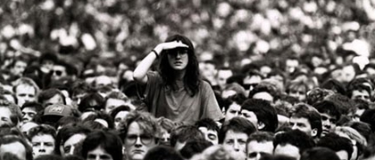 Woman standing head and shoulders above a sea of people shading her eyes from the sun looking around