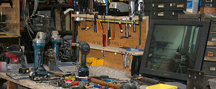 A workshop with screwdrivers, hammers, plyers, and hammers haphazardly laying around with an old computer monitor